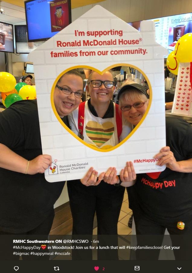 A group of three McDonald's employees posing inside a custom Ronald McDonald House cutout frame.